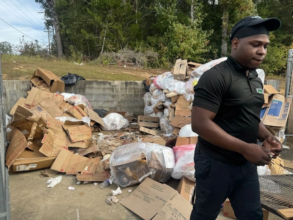 Person walking past a pile of cardboard and trash in a waste disposal area.